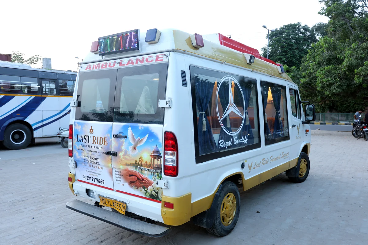 Rear three-quarter view of Last Ride Funeral premium hearse van with Last Ride Funeral Services branding, India Gate graphic, dove motif and 9217179989 helpline — Delhi